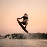 active strong man making trick in jump time with wakeboard on sky background. Summertime watersports activity