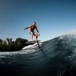 adult sportive man skillfully riding on the wave with hydrofoil foilboard on background of blue sky