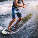 Active wakesurfer jumping on wake board down the river waves. Surfer on wave. Male athlete training on wakesurf training. Active water sports in open air on board. A man catches a wave on surf.